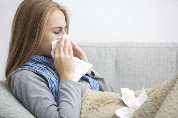 Women blowing her nose on the couch surrounded by used tissues