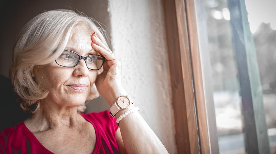 Older women with dementia standing in front of a window holding her head
