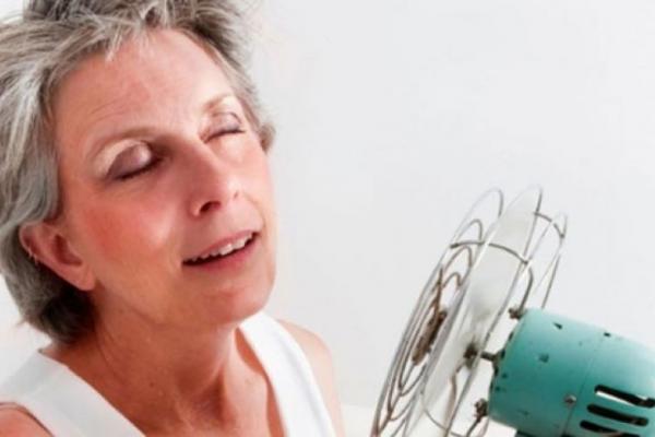 women facing hot flashes cools herself off in front of a fan