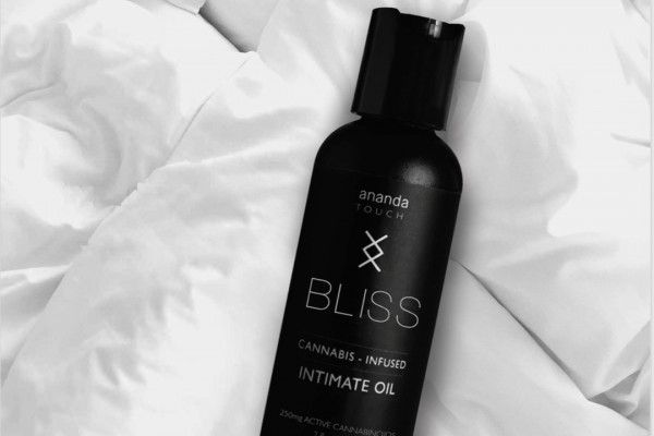 Bliss intimate oil placed on top of a white bed comforter
