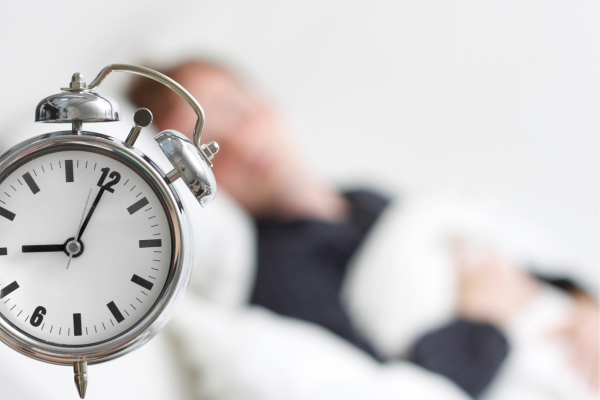 Man sleeping in a bed blurred out in the background of an alarm clock