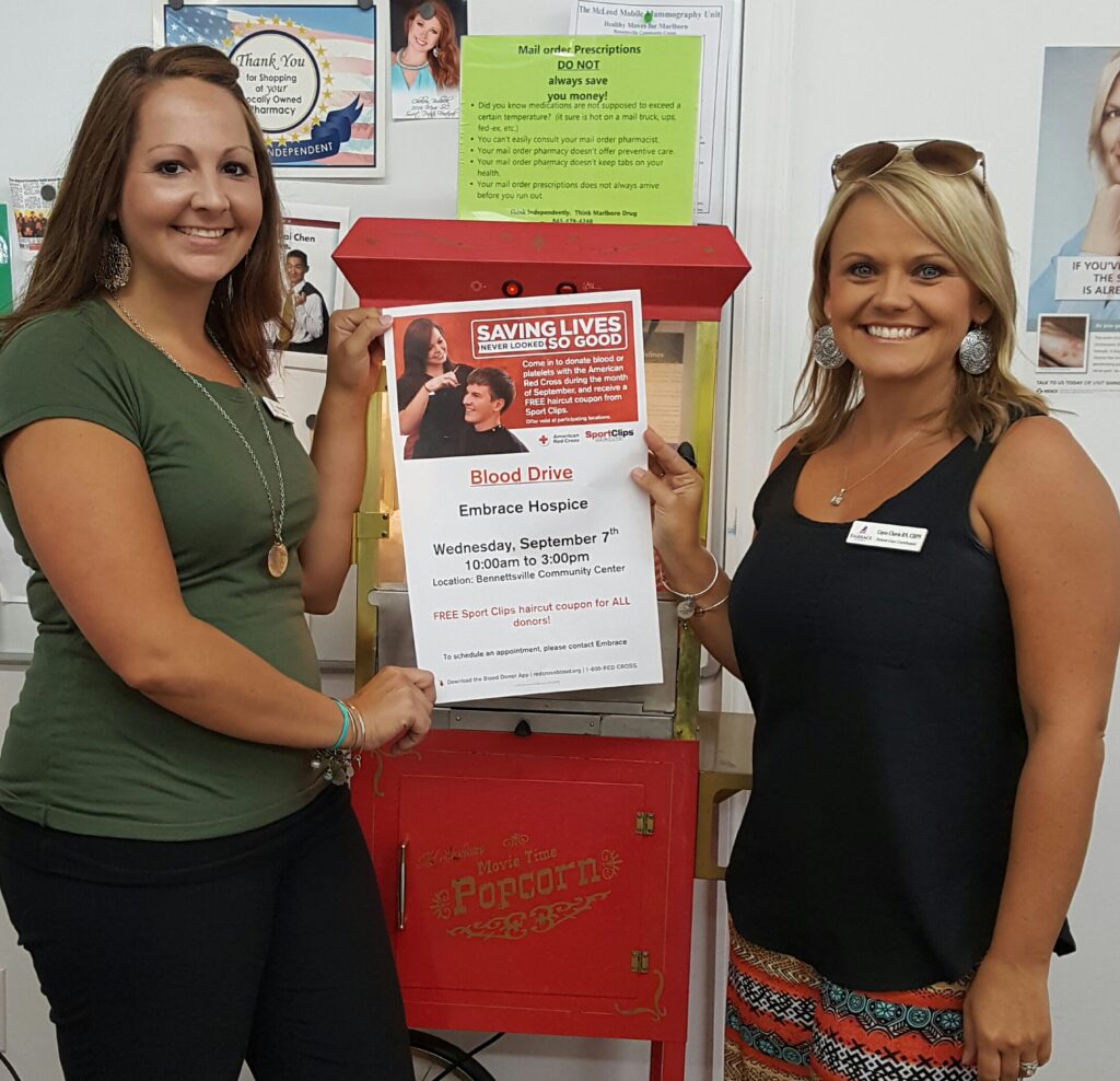 Two women holding a poster encouraging people to donate blood for a blood drive.